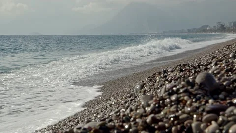 Small waves on shore of stone beach with city and mountains in background. Ocean Stock Footage 223612708