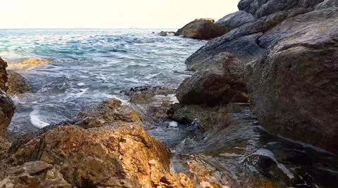 Small waves splashing on the rocks at sunset. Stock Photos