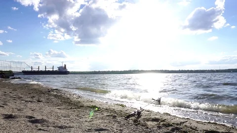 Small waves splashing on sand beach river shore as big cargo freight ship sails Stock-Footage 95225316