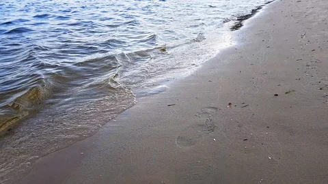 Small waves washing up a river shore with light brown sand in a sunny day. Stock Footage 112029181