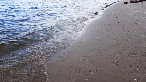 Small waves washing up a river shore with light brown sand in a sunny day. Stock Footage 112029491