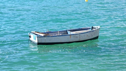 Small weathered rowboat floating on calm turquoise sea water near a yellow bu Vídeos de archivo 346799528