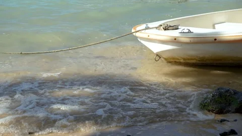 A small white boat is moored on a sandy beach, with gentle sea waves lapping the Stock Footage 311995841