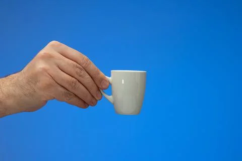 Small white ceramic coffee cup  held by Caucasian male hand. Close up studio  Fotos de archivo