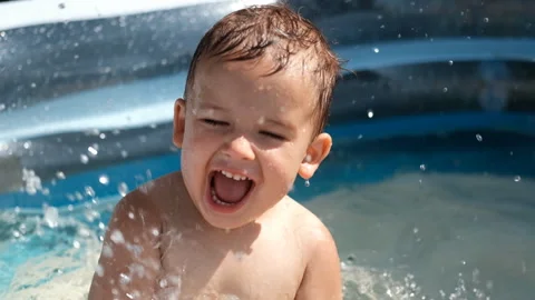 A small white child splashes in the pool in summer. Video stock 128181347