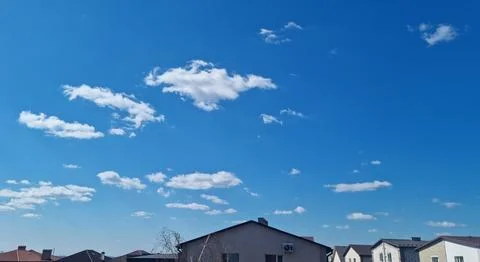 Small white clouds in blue sky over residential buildings. Stock Photos