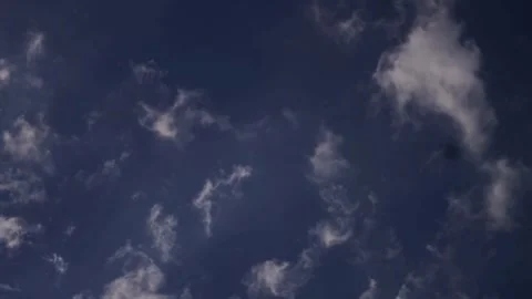 Small white clouds scatter across a deep blue sky Stock Footage 329756504