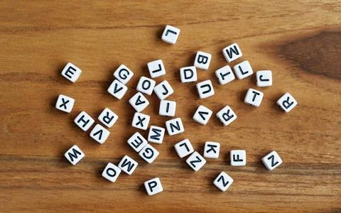 Small white cube beads with various letters scattered on wooden board, vie... Stock Photos