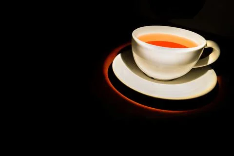 Small white cup filled with tea for health on black background. Stock Photos