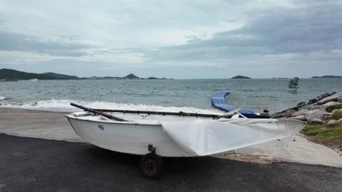 Small white dinghy boat on beach with sailboat sailing far away in sea Stock Footage 343198182