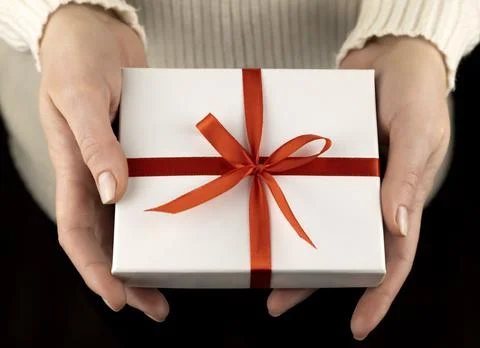 Small white gift box with red ribbon in beautiful female hands. 库存照片