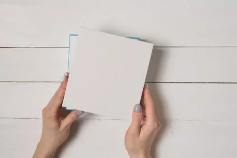 Small white half-open box in female hands. Top view. White table on the backg Foto stock