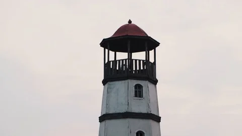 Small white lighthouse with a red top in the village with houses. Evening sunset Stock Footage 126881826