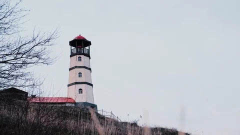Small white lighthouse with a red top along the seashore in an old village with  Stock Footage 126881882