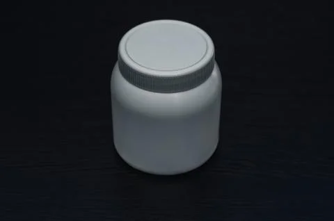A small white plastic jar on a black background Stock Photos