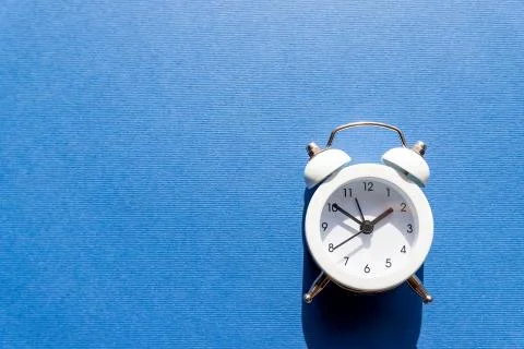 Small white retro clock isolated on blue background.Free time concept. Copy Foto stock