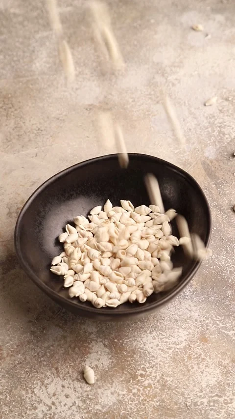 Small white seashells pour into a ceramic bowl on a brown concrete Video stock 221546287