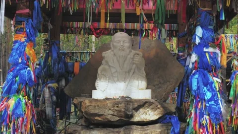 Small white statue of Buddha sitting on the stone surrounded with colorful Stock Footage 220107535