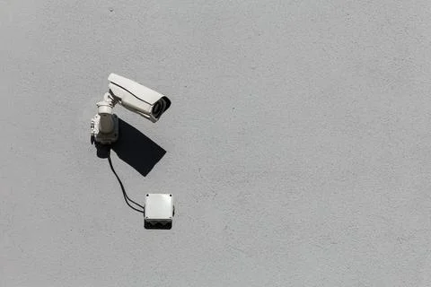 Small white surveillance camera on flat gray matte plaster wall Stock Photos