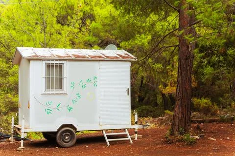 A small white trailer can be seen parked next to a tree in the woods Stock Photos