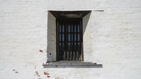 A small window with black bars on the background of a white brick wall. Stock Photos