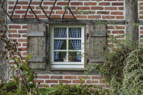 Small window with blue and white chequered curtains in a brick wall of a country Stock Photos