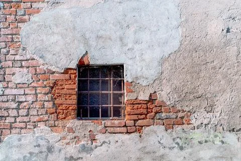Small window with a grid in an old brick wall and cracked dirty plaster. Stock Photos