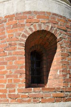 Small window in an old brick wall. Vaulted window with iron bars. Stock Photos