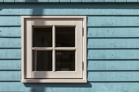 A small window of a tiny house with a white frame and light blue wooden facade 스톡 사진