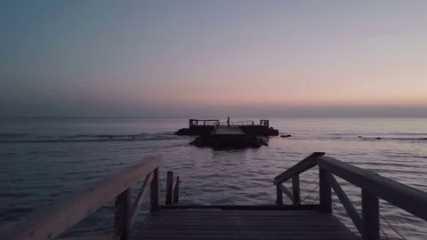 A small wooden bridge collapsed in the middle of the sea, autumn sunset. Aerial Stock Footage 70593381