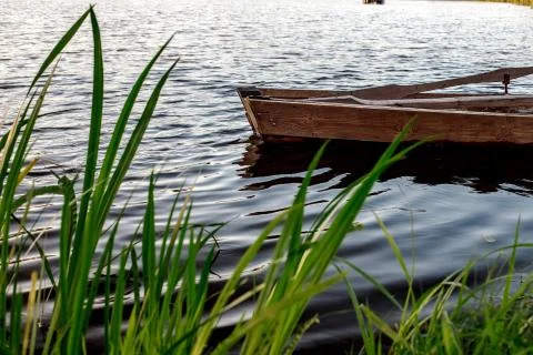 A small wooden rowing boat with a broken bottom on a calm lake near the shore Stock Photos