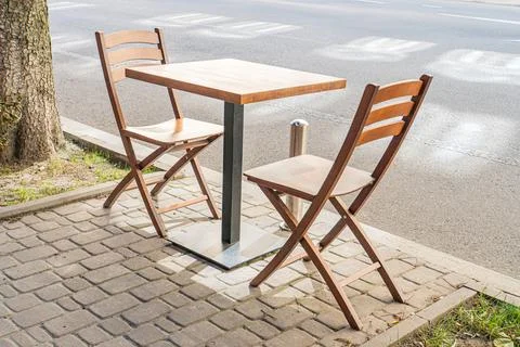 Small wooden table, light brown chairs with metal legs, urban brick paver s.. Stock Photos