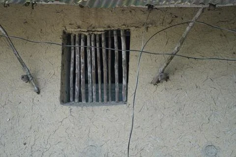 Small wooden window vent on a rustic mud wall in a rural village setting. Stock Photos