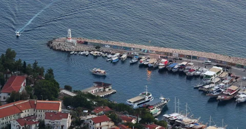 Small yachts enter harbor passing by lighthouse standing on breakwater. In Stock Footage 223957047