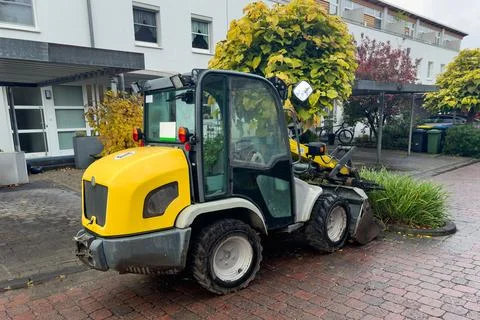 A small yellow backhoe loader standing on the sidewalk. Stock Photos