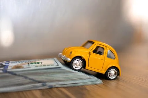 Small yellow car climbing a stack of money on a wooden surface during daylight Stock Photos