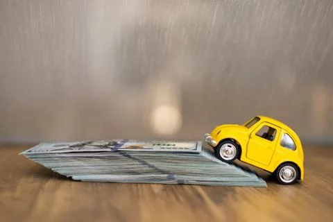 Small yellow car climbing a stack of money on a wooden surface during daylight Foto stock