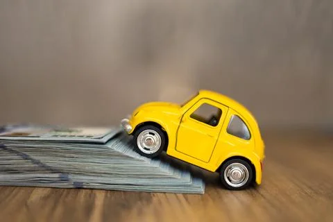 Small yellow car climbing a stack of money on a wooden surface during daylight Stock Photos