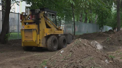 Small yellow excavator drives between across ground in park Stock Footage 325995553