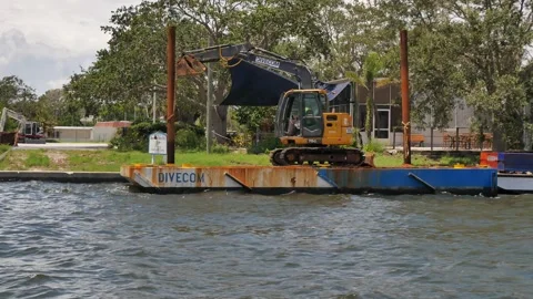 Small Yellow Excavator Operating on Floating Platform by a seawall. Compact exca Stock Footage 314808980