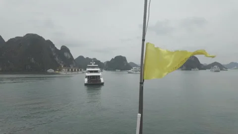 A small yellow flag flapping with cruise boat in background at ha long bay Vidéo 287526875