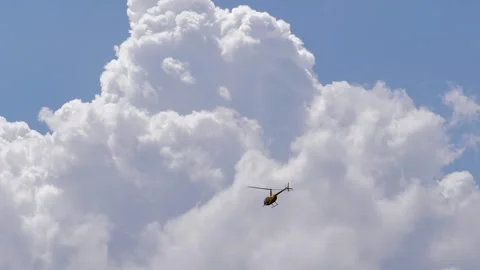 A small yellow helicopter flying against a backdrop of large white clouds Stock Footage 341933101