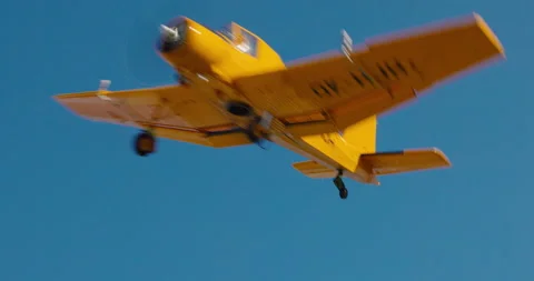 Small yellow propeller aircraft flying low over a dry grass field, 8K Stock Footage 339240375