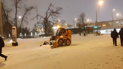 Small yellow snowplow clears heavy snowfall on urban pathway early morning. City Stockbeeldmateriaal 327126482