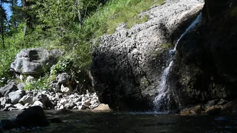 A smaller waterfall in sunlight next to a mountain stream (slow motion) Stock-Footage 219418767