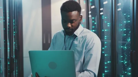 Smart african IT administrator using notebook computer inspecting working server Video stock 119232239