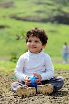 Smart and cute looking boy is sittng on the ground on a hill. On a Sunny day  Stock Photos