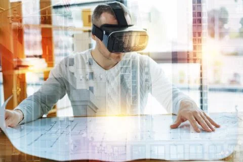 Smart architect sitting with a drawing while wearing virtual reality glasses Foto stock
