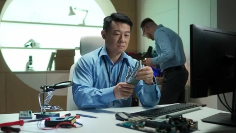 Smart Asian creator sitting in front of computer and holding robots hand Stock Footage 241240710