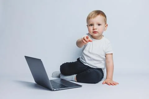 A smart boy 3-4 years old sits with a laptop on a white background. A child i 库存照片